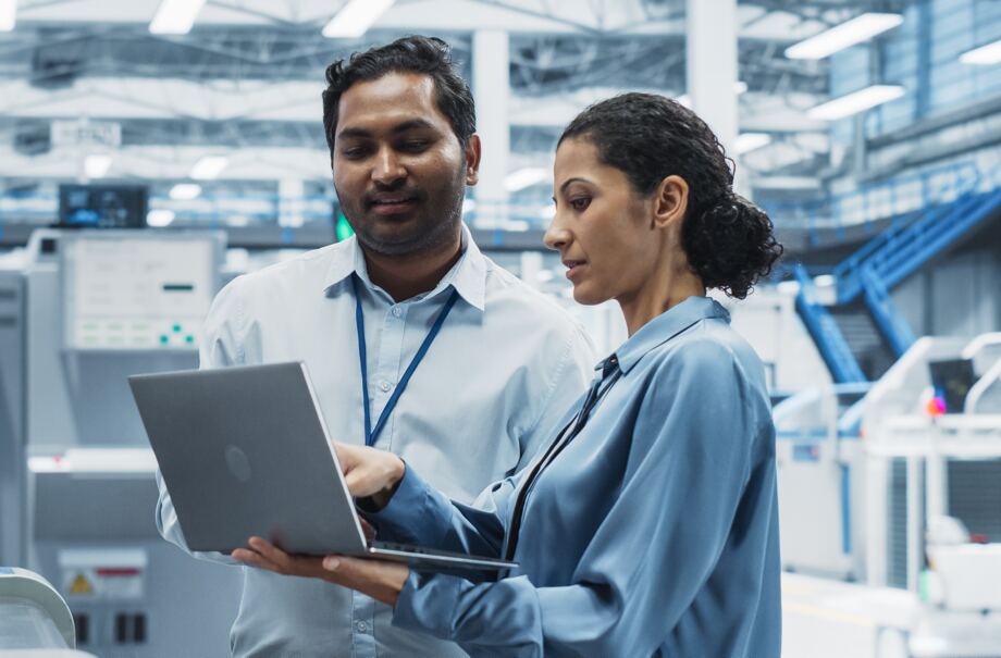 Two engineers reviewing work on a laptop in a production facility